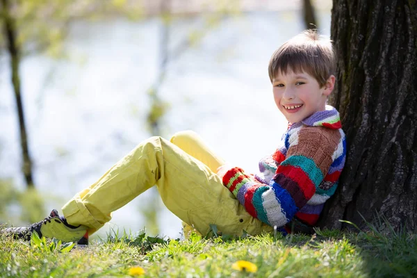 Il bambino è seduto sull'erba. Ragazzo felice in una passeggiata nel parco. — Foto Stock