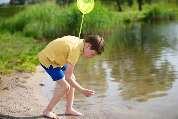 El chico está pescando con una red de mariposas en el lago. — Foto de Stock