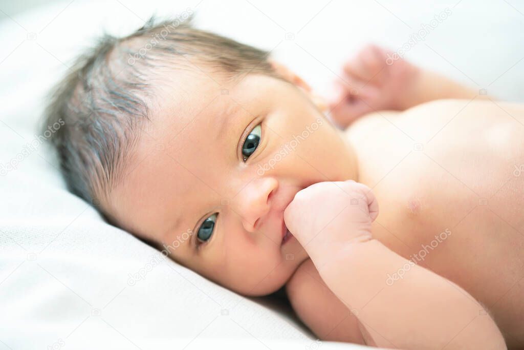 Newborn baby with open eyes sucks on a cam.