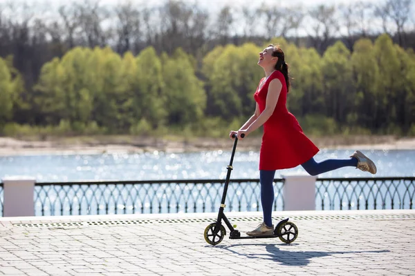 Una mujer adulta está montando un scooter en la calle. Mujer activa de mediana edad en un paseo. — Foto de Stock