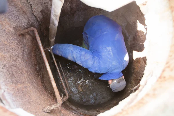 Worker cleans the sewer hatch.A worker cleans a sewer hatch. A man in the hatch.