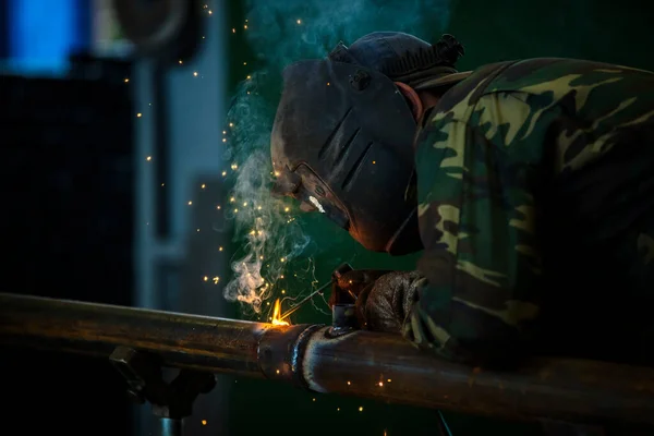 Hegesztő munka közben. Védőmaszkos férfi. A hegesztő varratokat készít a fémen. Hegesztéskor szikrák és füst. — Stock Fotó