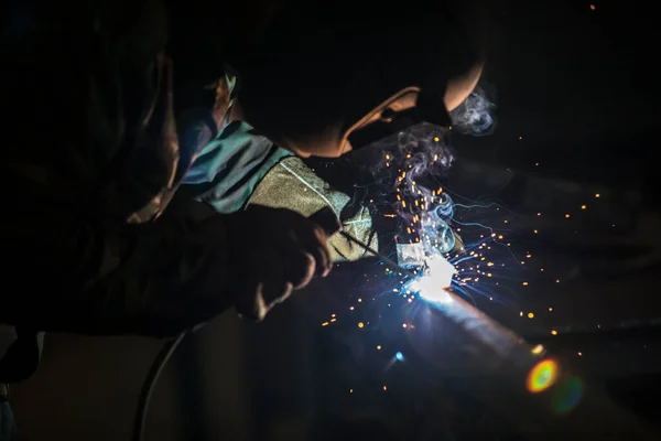 焊接工人在工作。戴着防护面具的男人焊机在金属上焊接.焊接时的火花和烟雾. — 图库照片