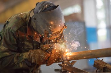 Kaynakçı işte. Koruyucu maskeli adam. Kaynakçı metalde dikişler yapıyor. Kaynak yaparken kıvılcım ve duman.