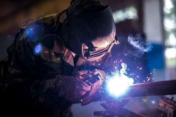 Hegesztő munka közben. Védőmaszkos férfi. A hegesztő varratokat készít a fémen. Hegesztéskor szikrák és füst. — Stock Fotó