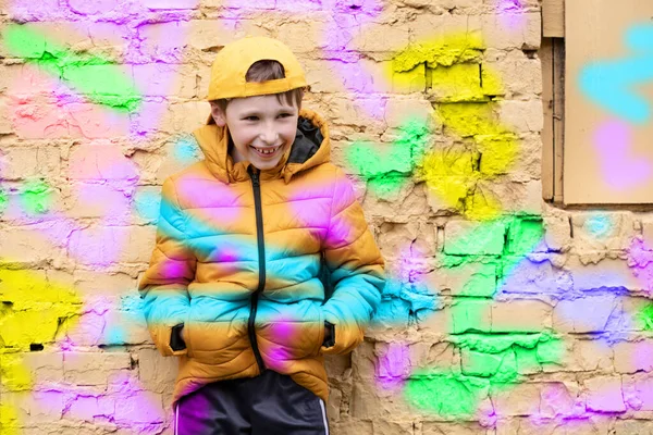 Παιδί με γκράφιτι. Το αγόρι στέκεται σε έναν τοίχο από τούβλα με μοντέρνα ρούχα και ένα καπέλο του μπέιζμπολ, σκιαγραφείται με φωτεινά χρώματα. — Φωτογραφία Αρχείου