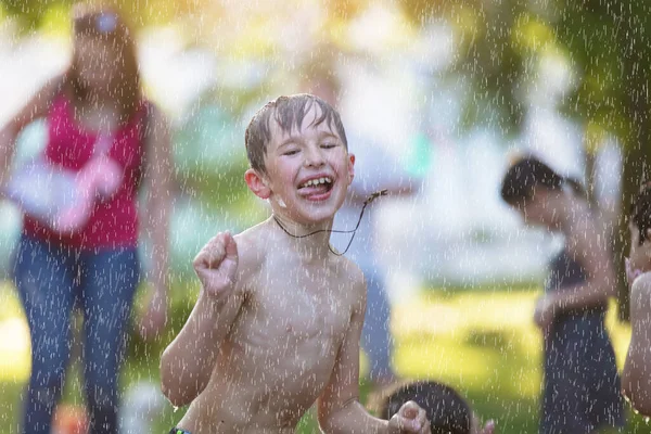 Ragazzino sotto i getti d'acqua. Un bambino sotto la pioggia battente. . Vai sotto la cascata. Bagno nella fontana della città. — Foto Stock