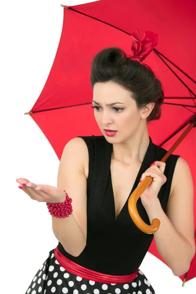 Uma garota retro pinup com um guarda-chuva vermelho assistindo a chuva. — Fotografia de Stock