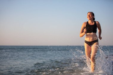 Orta yaşlı bir kadın kıyı boyunca koşar. Denizde spor yapıyor..