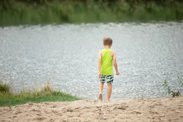 Kind aan de oevers van de rivier achteraanzicht. Een jongen bij de vijver. — Stockfoto