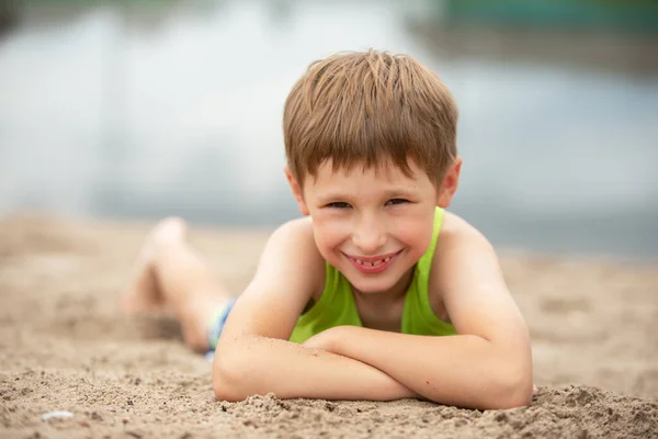 Piccolo bambino allegro nella sabbia vicino all'acqua. Ritratto di un ragazzo in abiti estivi sulla spiaggia. — Foto Stock