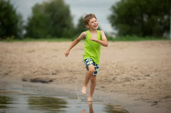 El chico feliz corre por la playa. Un niño juega junto al río. — Foto de Stock