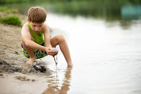 Ein Kind spielt mit dem Sand an der Küste. Ein Junge am Wasser am See. — Stockfoto