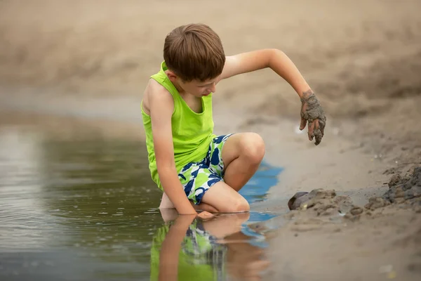 Un bambino gioca con la sabbia sulle rive del fiume. — Foto Stock