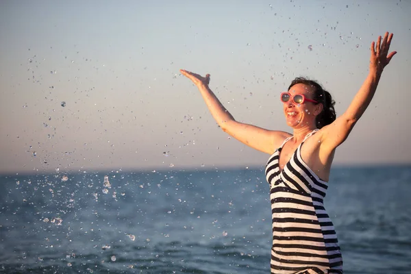海で美しい老婦人。美しい中年女性が海の水を振りかける. — ストック写真