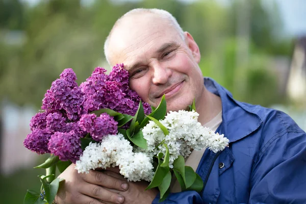 Hombre mayor con un ramo de flores. Brutal hombre de pelo gris con una hermosa lila. — Foto de Stock