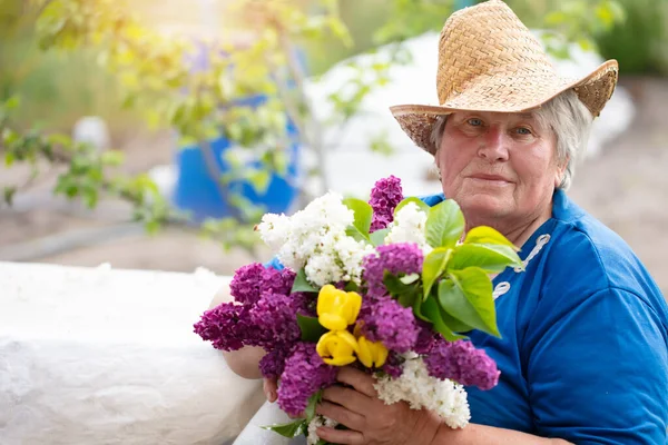 Mujer de pelo gris hermosa anciana con un ramo de lilas al aire libre. Pensionista en el país. — Foto de Stock