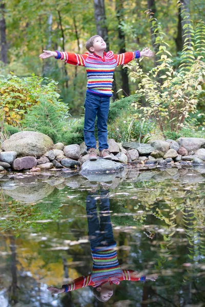 Bambino in una passeggiata autunnale. Ragazzo in piedi con un maglione caldo vicino al lago d'autunno. — Foto Stock