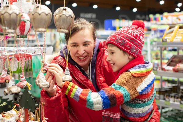 Mamá con un hijo en la venta de Navidad. Los compradores contentos en el mercado de Navidad eligen productos. — Foto de Stock