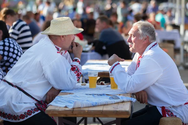 08 29 2020 Belarus, Lyaskovichi. Şehirde bir tatil. Ulusal Slav şapkalı adamlar bir masada oturuyorlar..