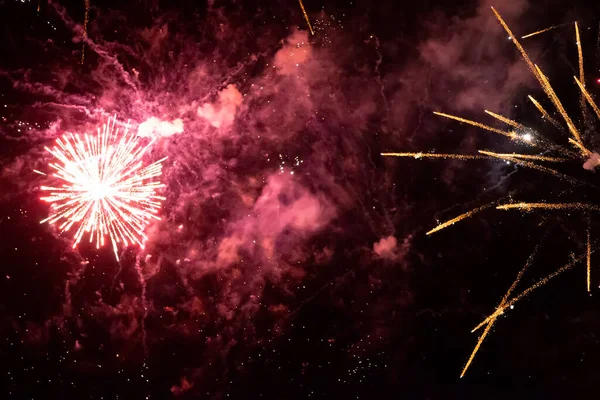 Raios de ouro de fogos de artifício em fumaça vermelha em um fundo preto. Fundo festivo. — Fotografia de Stock