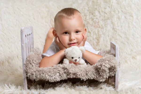 Lindo niño pequeño con un juguete suave se encuentra en una cama de juguete. Niño de tres años con un fondo esponjoso. — Foto de Stock