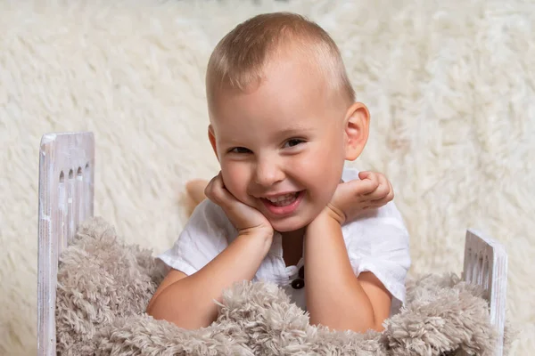 Lindo bebé en una cama de juguete. Niño alegre de tres años con una sonrisa. — Foto de Stock