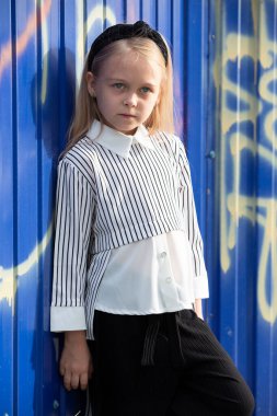 İlkokul çağında güzel bir kız üzerinde grafiti olan mavi bir duvarın yanında duruyor..