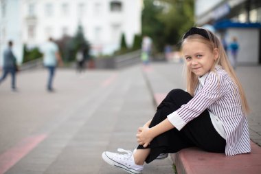 Şehir ortamında güzel küçük bir kız. Çocuk mağazanın önündeki merdivenlerde oturur..
