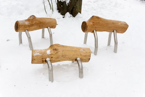 Walking logs. Interesting benches in the form of unusual animals made of wood in the snow. Benches in the form of sheep. Winter landscape.