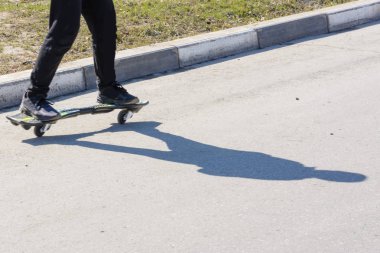 Asfaltta dalga tahtasına binen adam. Yolda kaykay türü ve bir adamın ayakları. Kaldırımda gölge.