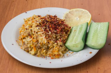 Iştah açıcı, lezzetli, sıcak, taze pilav iki salatalık ve limon bir dilim ile bir tabak ta. Sığır eti, havuç, soğan, ahşap arka plan üzerinde sarımsak ile Pilav. Geleneksel bir yemek Asya.