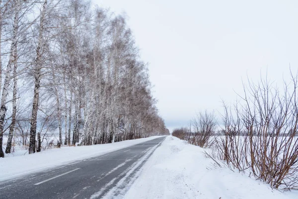 Patterns on the winter highway in the form of four straight lines. Snowy road on the background of snow-covered forest. Winter landscape.