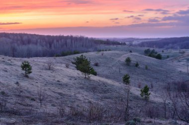 Güzel bahar manzara: gün batımı, ağaçlar, orman, dağlar, tepeler, tarlalar, çayırlar ve gökyüzü. Gün batımında ağır bulutlarla muhteşem, kırmızı gökyüzü. Bahar.