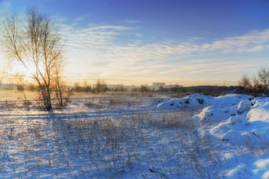 Kış manzarası. Gün batımı, şehir manzarası ve kule vinç bir arka plan üzerinde dondurulmuş alan. Parlak bulutlar.