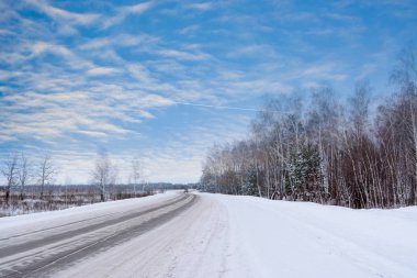 Kış otobanı üzerindeki şablonlar dört düz çizgi şeklinde. Karla kaplı ormanın arka planında karlı bir yol. Kış manzarası.