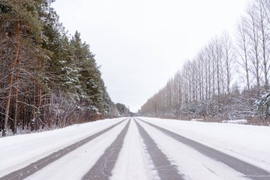 Kış otobanı üzerindeki şablonlar dört düz çizgi şeklinde. Karla kaplı ormanın arka planında karlı bir yol. Kış manzarası.