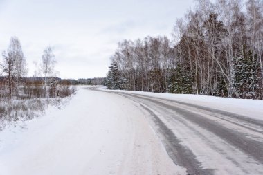 Kış otobanı üzerindeki şablonlar dört düz çizgi şeklinde. Karla kaplı ormanın arka planında karlı bir yol. Kış manzarası.
