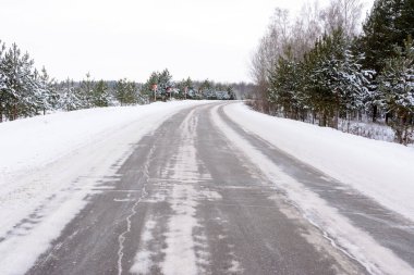 Kış otobanı üzerindeki şablonlar dört düz çizgi şeklinde. Karla kaplı ormanın arka planında karlı bir yol. Kış manzarası.