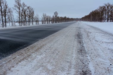 Otobanda kar fırtınası. Kış otobanı üzerindeki şablonlar dört düz çizgi şeklinde. Karla kaplı ormanın arka planında karlı bir yol.