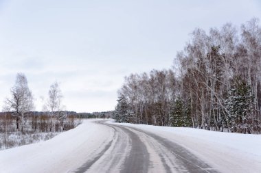Kış otobanı üzerindeki şablonlar dört düz çizgi şeklinde. Karla kaplı ormanın arka planında karlı bir yol. Kış manzarası.