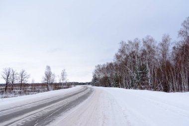 Kış otobanı üzerindeki şablonlar dört düz çizgi şeklinde. Karla kaplı ormanın arka planında karlı bir yol. Kış manzarası.