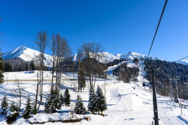Teleferiği, dağ yamacı ve kayakçıları olan kış manzarası. Karla kaplı dağ zirveleri kış etkinlikleri için etkileyici bir zemin oluşturur..