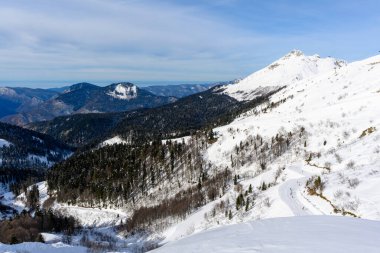Kayak pistinin tepesinden karla kaplı dağların net bir manzarası. Dağ sıraları uzaklığa uzanırken yamaçlar kayakçılarla doludur..