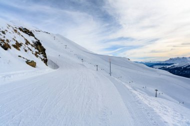 Karlı dağ yamaçları, kayak pistlerinin ve teleferiklerin manzarası. Önde karla kaplı zirveler, ufukta görkemli dağlar..