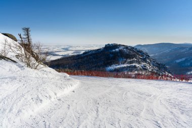 Abzakovo köyü yakınlarındaki güneşli bir kış gününde, Ural Dağları manzarasının zemininde kırmızı kısıtlayıcı ağ bulunan dik kayak yamacı. Aktif yaşam tarzı ve açık hava seyahat kavramı.