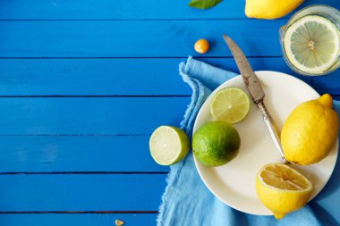  Limes ve limon dilimleri ile plaka ve masa örtüsü mavi ahşap arka plan, limonata malzemeleri kavramı üzerinde 