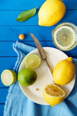 Limes ve limon dilimleri ile plaka ve masa örtüsü mavi ahşap arka plan, limonata malzemeleri kavramı üzerinde 