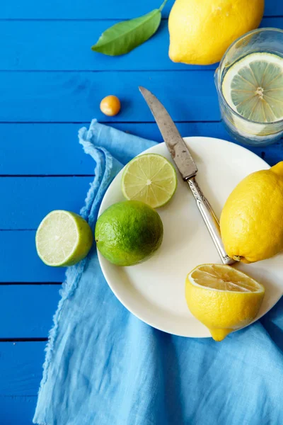 Limes ve limon dilimleri ile plaka ve masa örtüsü mavi ahşap arka plan, limonata malzemeleri kavramı üzerinde 