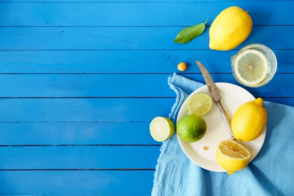  Limes ve limon dilimleri ile plaka ve masa örtüsü mavi ahşap arka plan, limonata malzemeleri kavramı üzerinde 